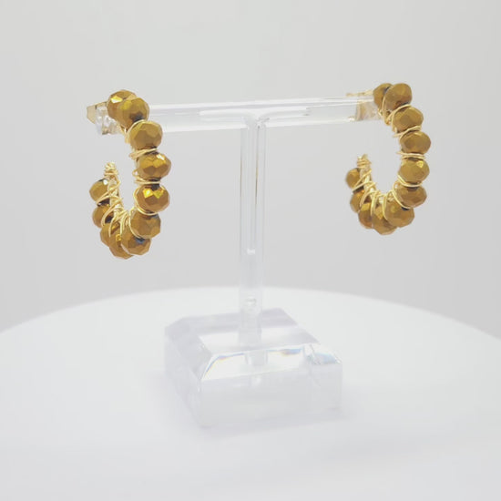 Video of golden hoops with delicate chocolate faceted rondelle glass beads, both standing on a white base rotating counterclockwise
