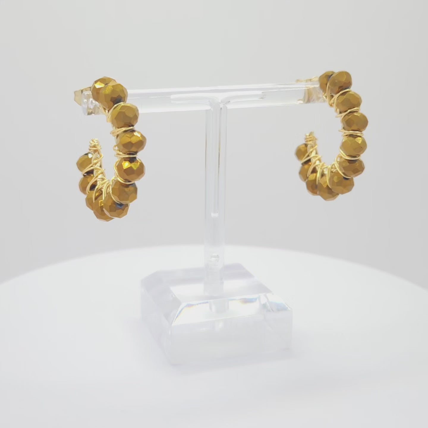 Video of golden hoops with delicate chocolate faceted rondelle glass beads, both standing on a white base rotating counterclockwise