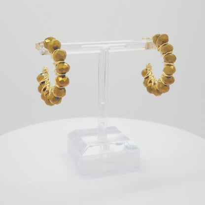 Video of golden hoops with delicate chocolate faceted rondelle glass beads, both standing on a white base rotating counterclockwise