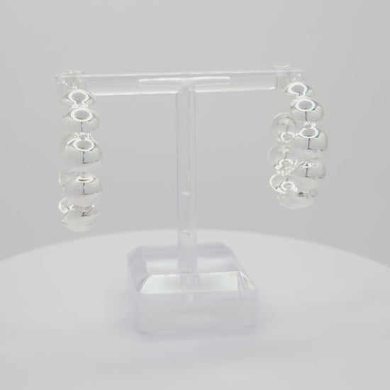 Video of silver hoops with flat spheres, both standing on a white base rotating counterclockwise