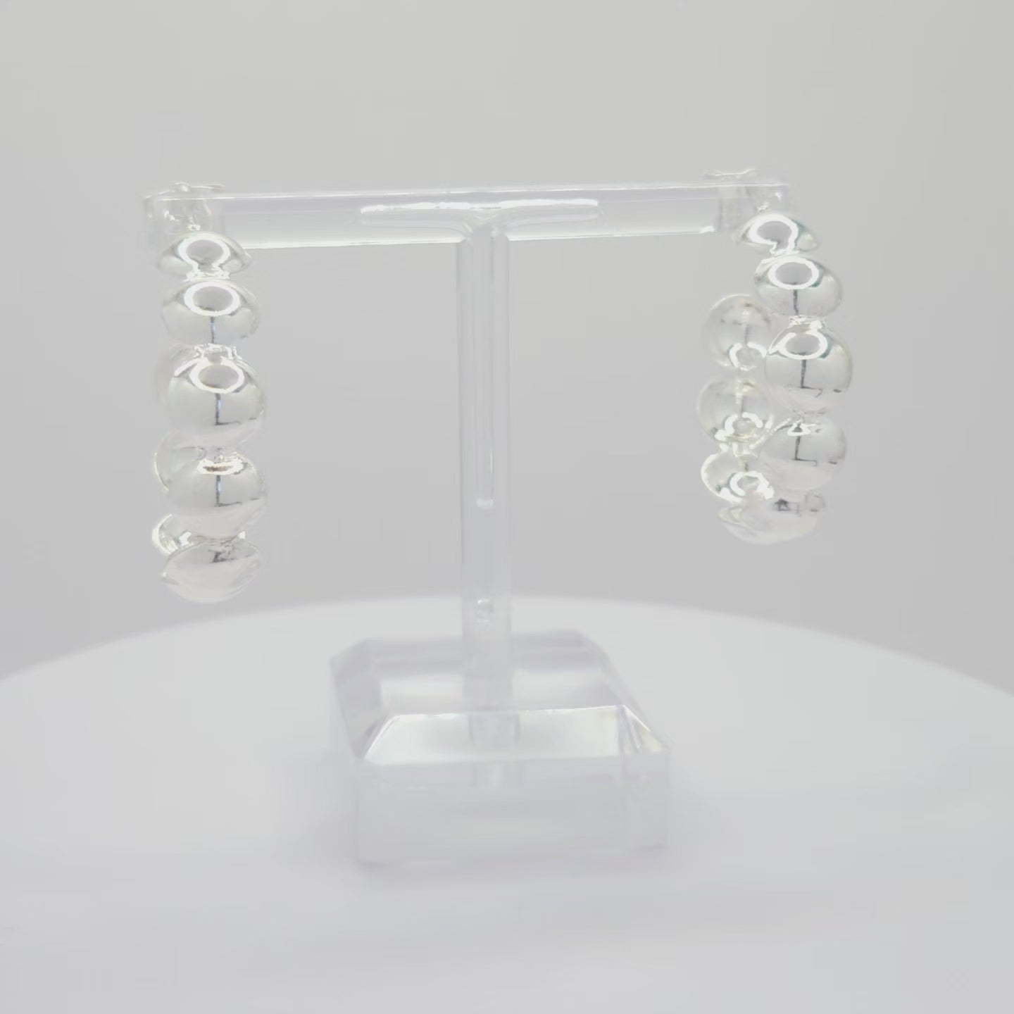 Video of silver hoops with flat spheres, both standing on a white base rotating counterclockwise