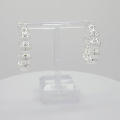 Video of silver hoops with flat spheres, both standing on a white base rotating counterclockwise