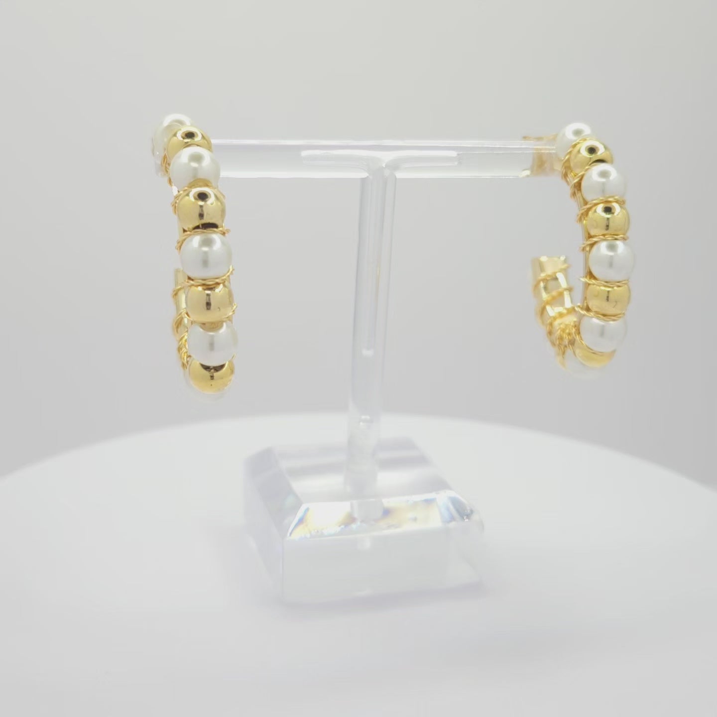 Video of golden hoops with pearls and golden spheres, both standing on a white base rotating counterclockwise
