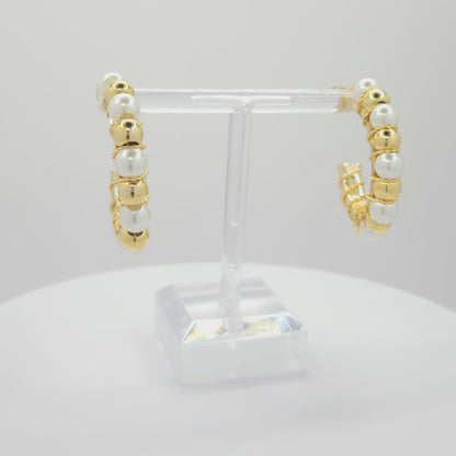 Video of golden hoops with pearls and golden spheres, both standing on a white base rotating counterclockwise