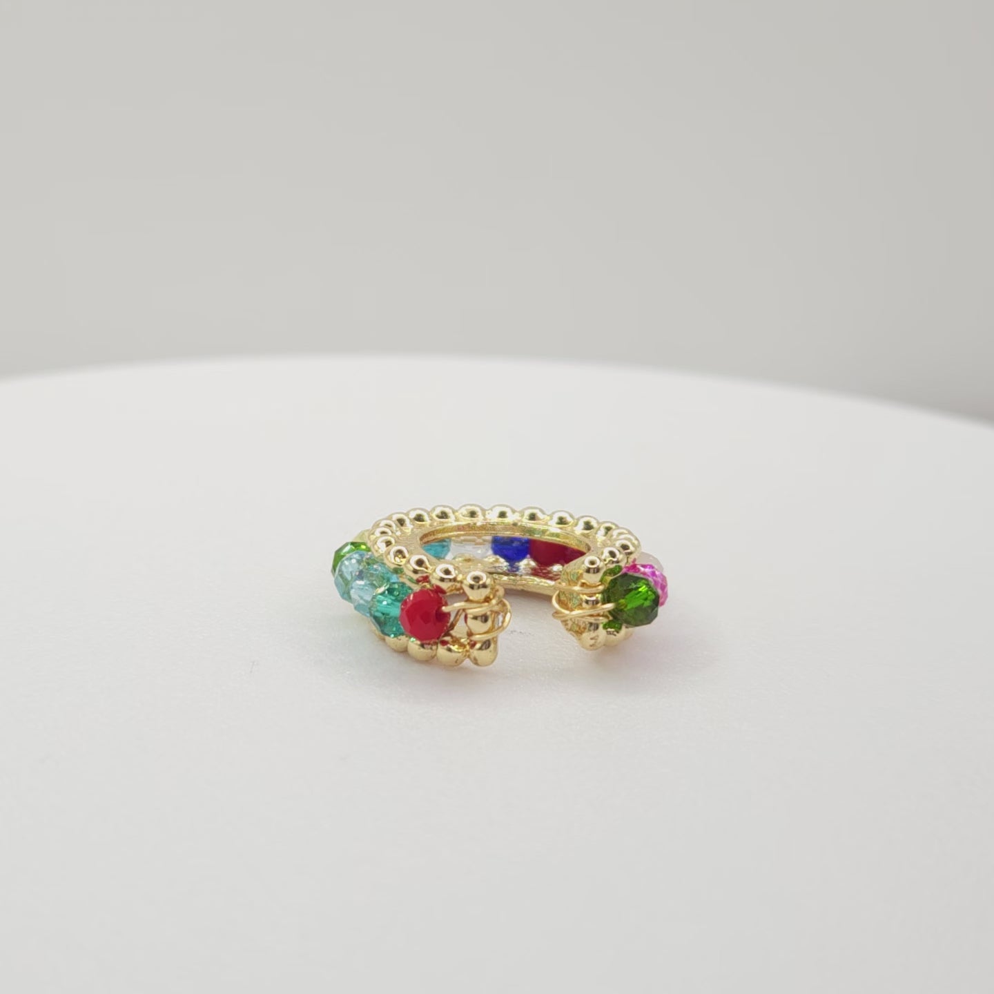 Video of a golden ear cuff featuring an array of multicolour faceted rondelle glass beads lying on a white base, rotating counterclockwise