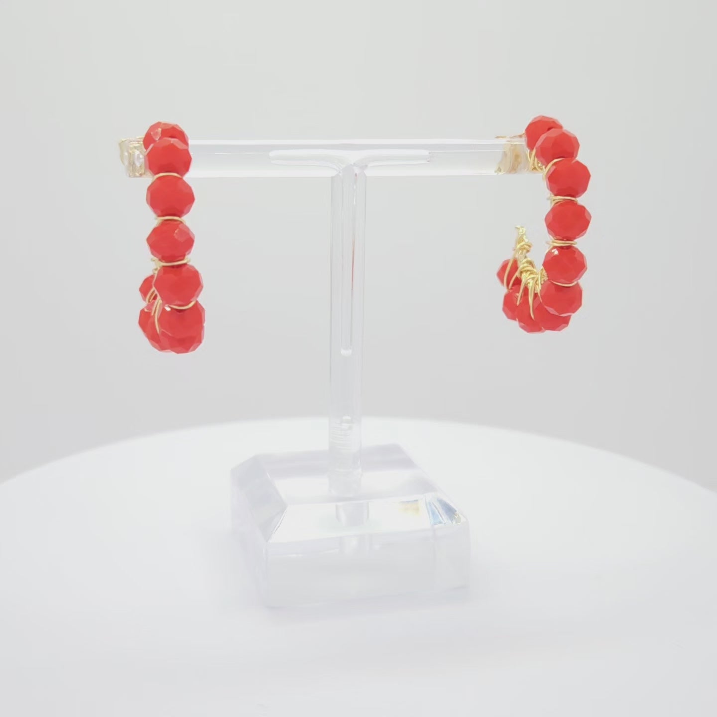 Video of golden hoops with delicate red faceted rondelle glass beads, both standing on a white base rotating counterclockwise