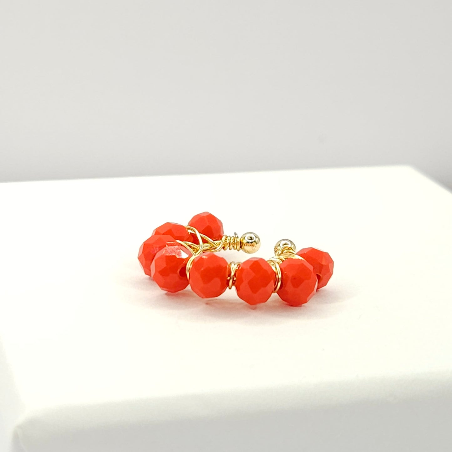 Golden ear cuff adorned with a delicate weave of red faceted rondelle glass beads lying on a white base
