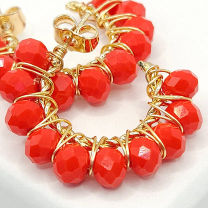 Close-up of golden hoops with red faceted rondelle beads, focused on lower right details, blurring toward upper left corner