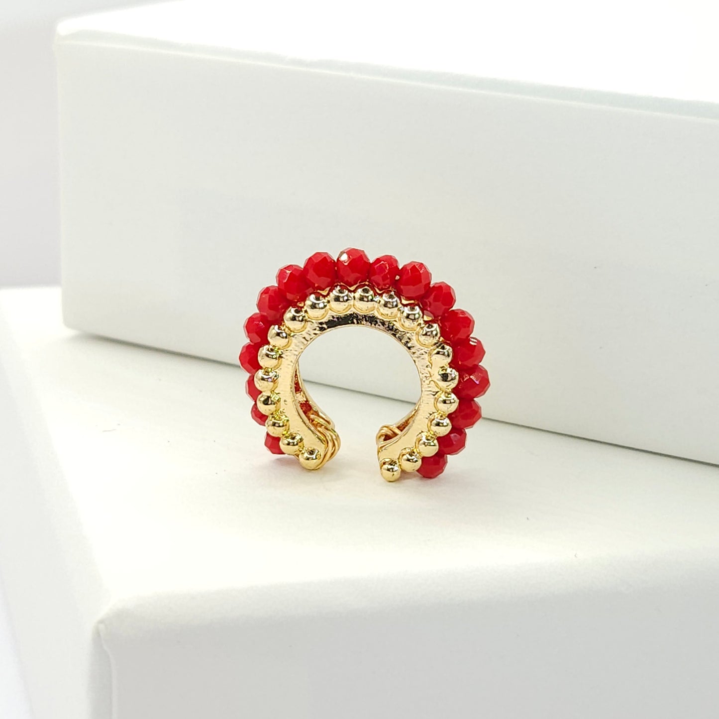 Golden ear cuff featuring an array of red faceted rondelle glass beads standing on a white base