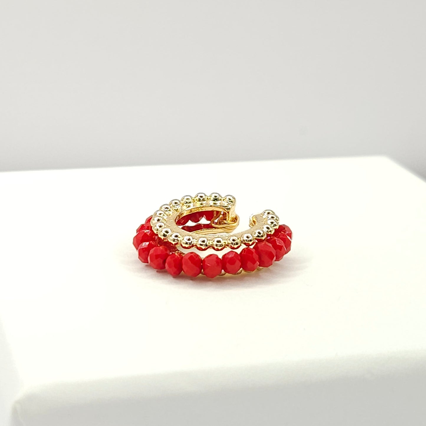 Golden ear cuff featuring an array of red faceted rondelle glass beads lying on a white base