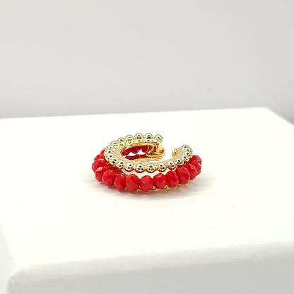 Golden ear cuff featuring an array of red faceted rondelle glass beads lying on a white base