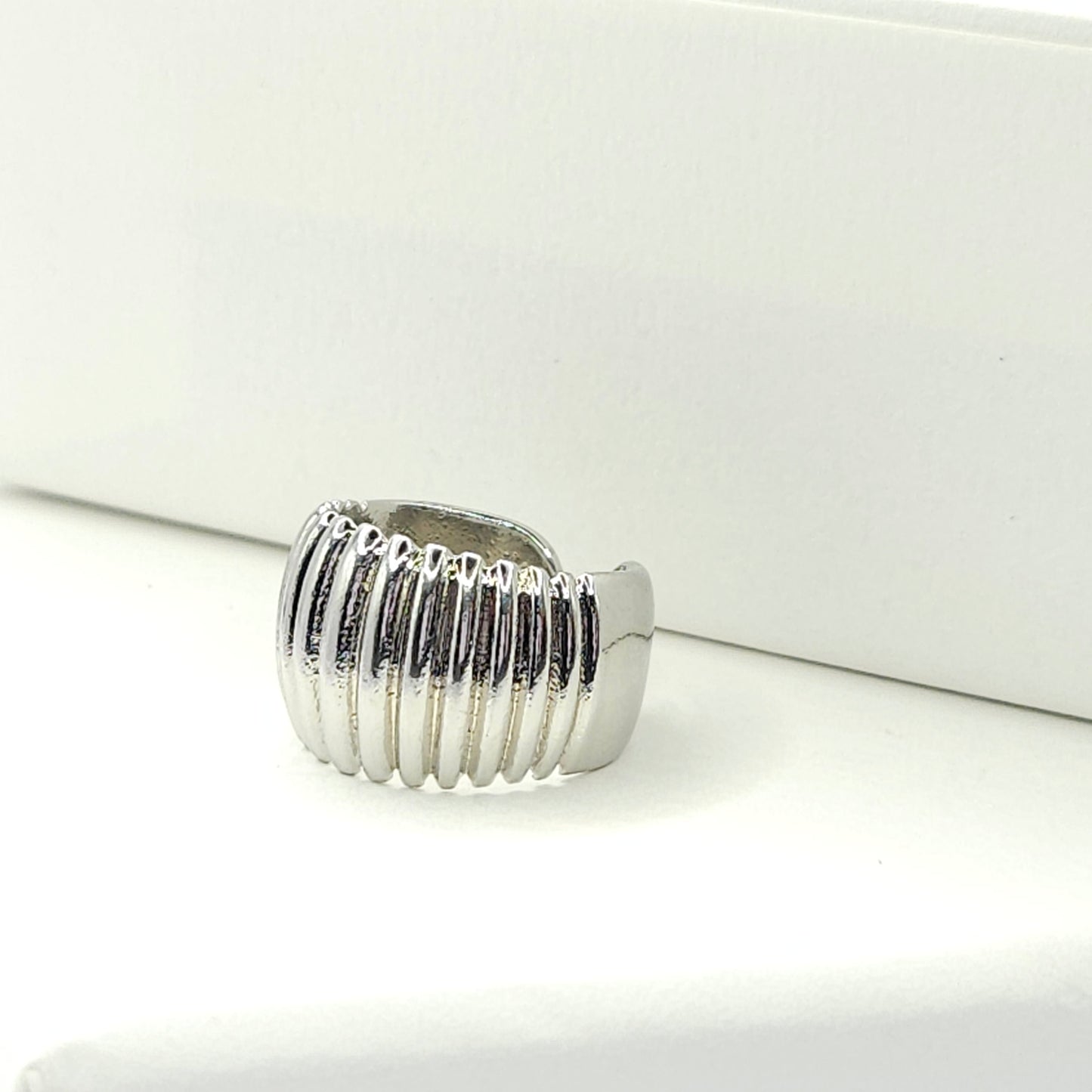 Silver ear cuff adorned with subtle stripes lying on a white base
